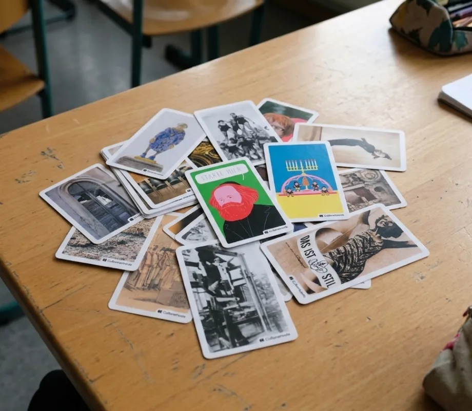 Tacheles-Karten liegen verstreut auf einem Schultisch, daneben Federmäppchen mit Buntstiften und ein beschriebenes Heft.
